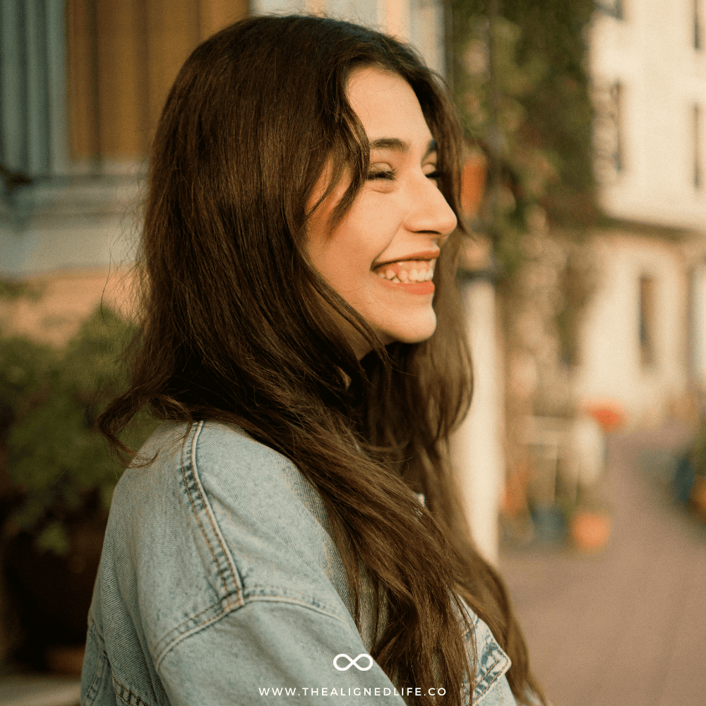 brunette woman in denim jacket smiling | How To Let Go To Manifest | The Aligned Life Manifestation Blog
