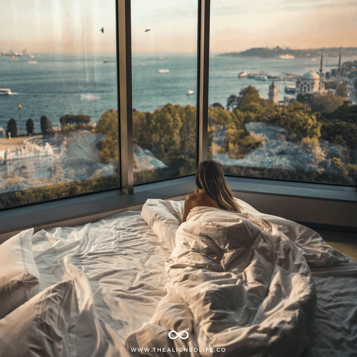 woman in a bed looking out at the beach | 100 Things To Manifest | The Aligned Life Manifestation Blog