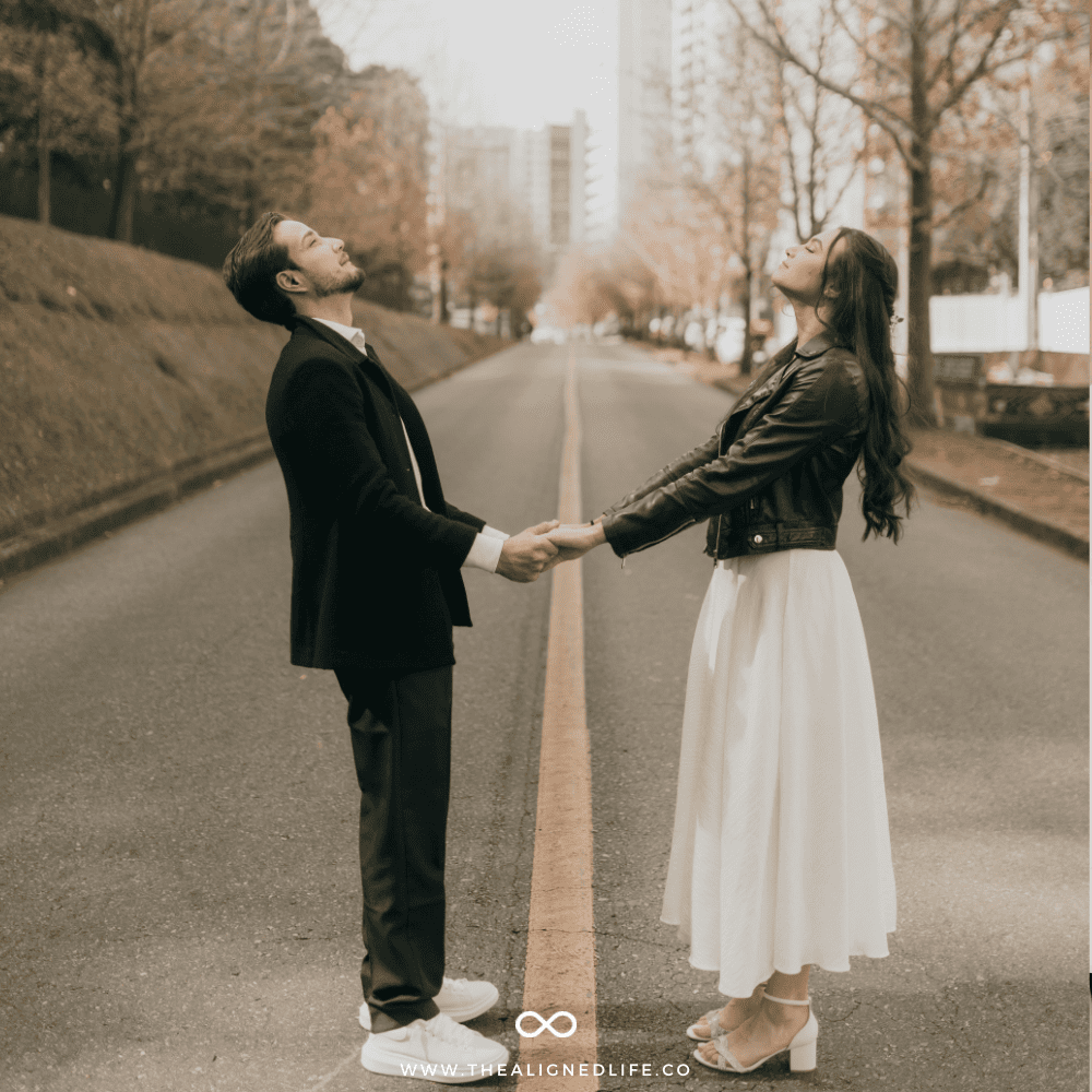 man and woman holding hands in a road with tall city buildings and trees behind them | How To Manifest A Relationship | The Aligned Life Manifestation Blog