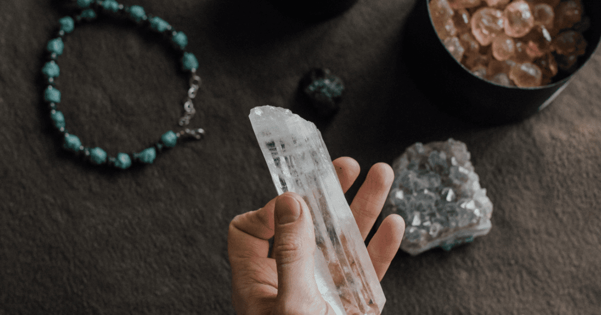 hand over a dark wood table holding a crystal | How To Cleanse, Charge & Program Crystals | The Aligned Life Manifestation Blog