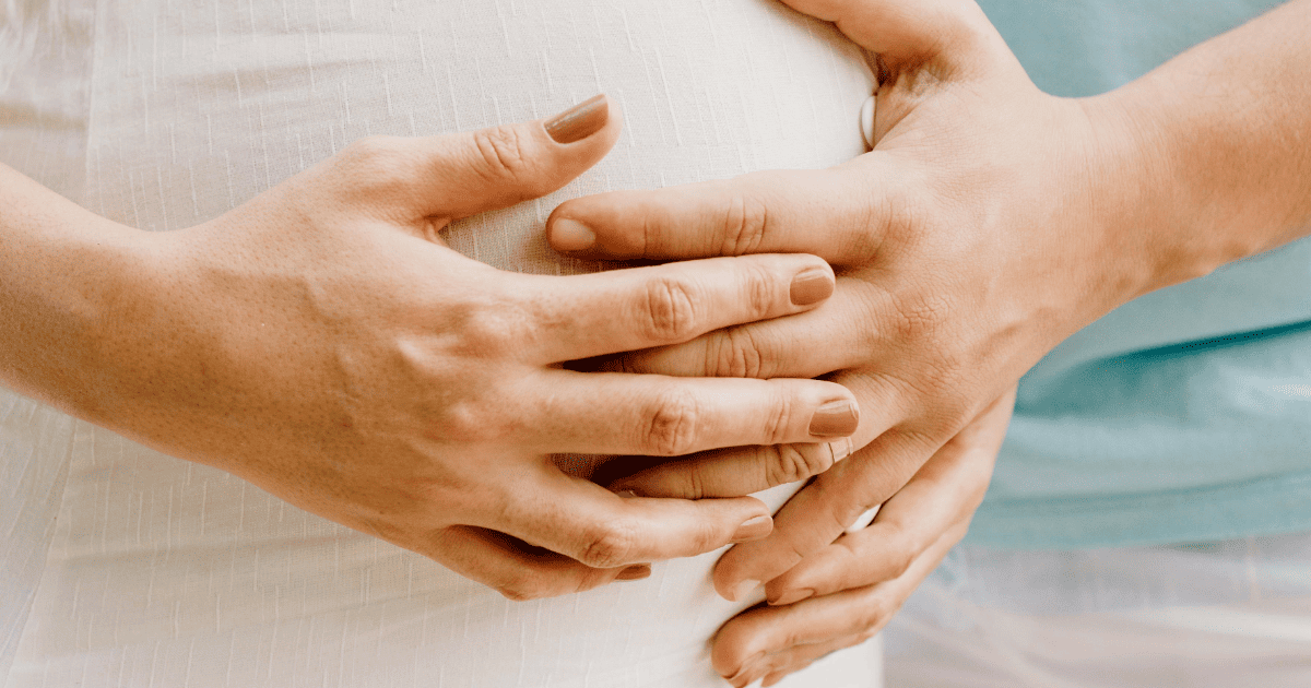 woman in a white dress with hands on a pregnant belly | How To Manifest A Baby | The Aligned Life Manifestation Blog