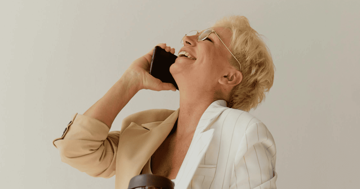 blonde woman in a beige jacket laughing on a cellphone | How To Manifest Your Dream Job | The Aligned Life Manifestation Blog