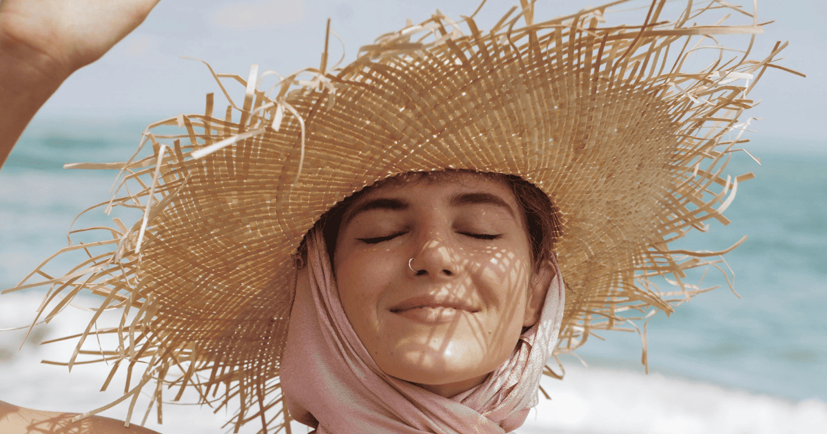 woman smiling in a straw hat on the beach | How to Break Through Your Manifestation Blocks | The Aligned Life Manifestation Blog