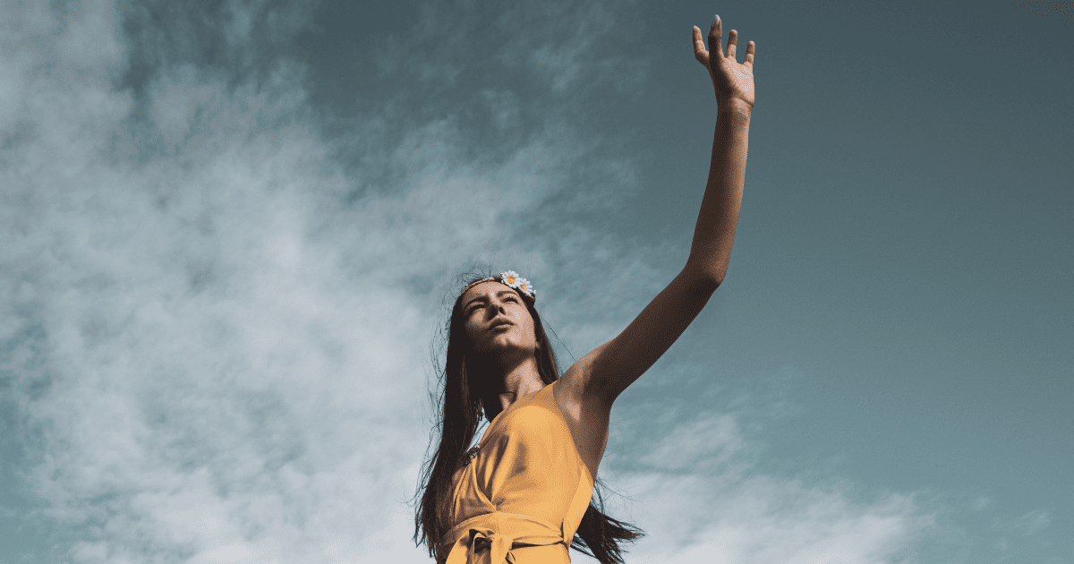 woman in a yellow dress with her hand against the sky | How To Use The 21 Universal Laws | The Aligned Life Manifestation Blog
