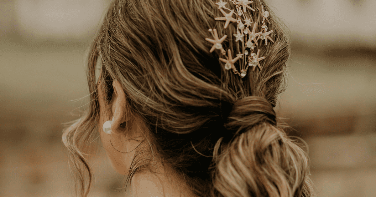 blonde woman facing away from camera with seashells in her hair