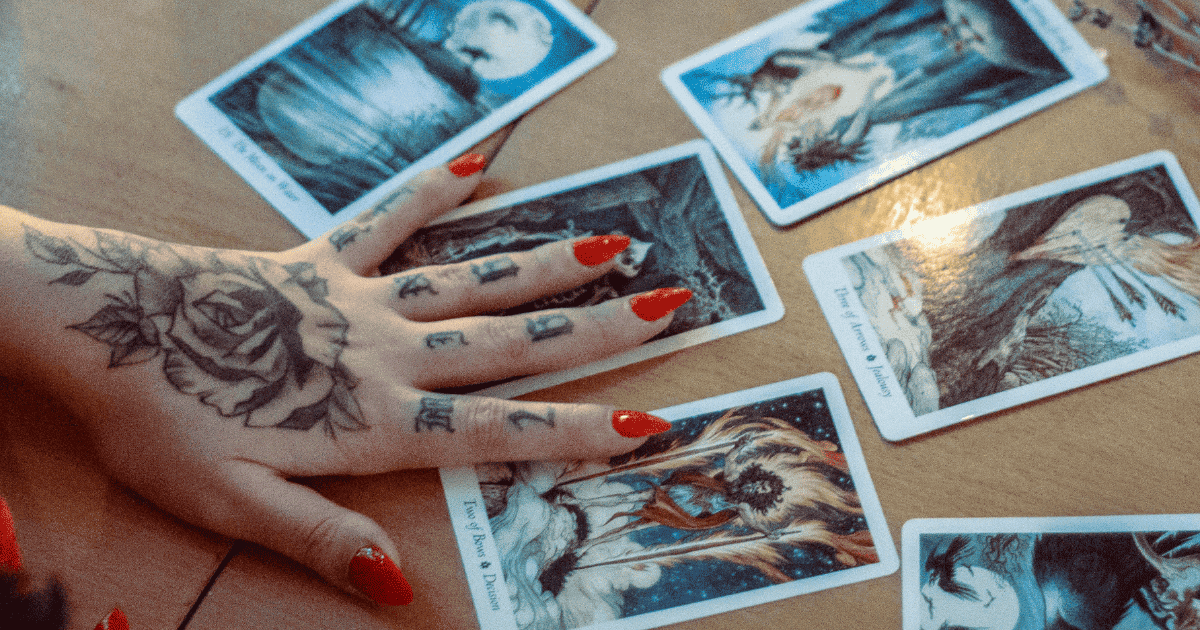 tattooed arm and hand on a tarot card spread What Tarot Card Is Your Zodiac Sign?