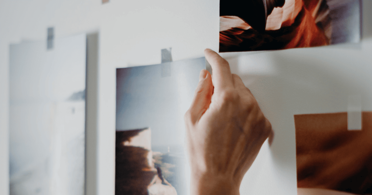 a woman's hands taping a picture to a white wall | How To Make A Vision Board In 2026 For Manifestation