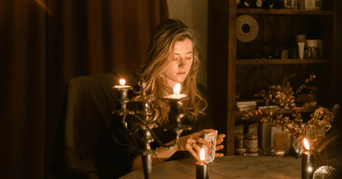 blonde woman sits holding tarot cards surrounded by candles | 9 Rituals For Winter Solstice