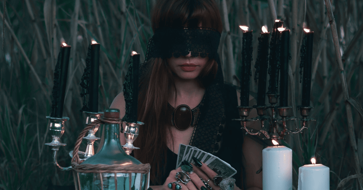 woman sitting in grass with a blindfold, candles and tarot cards | The Manifestation Group Spell